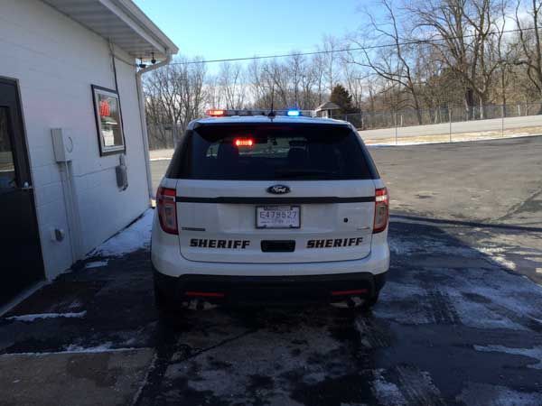 Rear view of a white Sheriff's Ford Explorer parked near a building, with flashing red and blue lights activated.