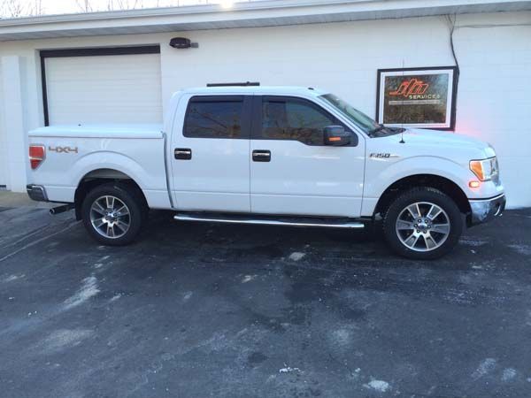 White Ford F-150 pickup truck parked outside a building with a closed garage door and business sign.