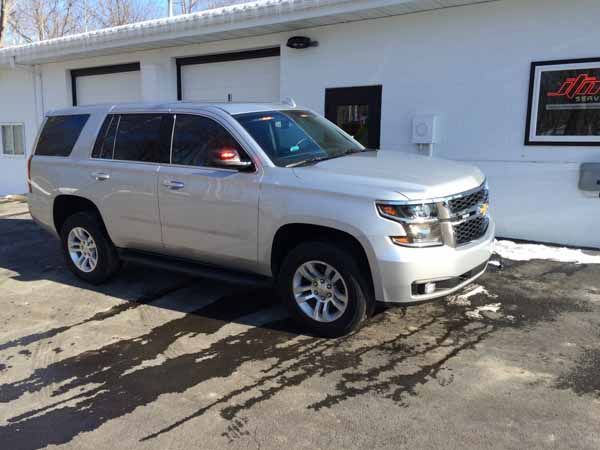 Silver Chevrolet Tahoe SUV parked outside a white building with black doors. Sunny day.