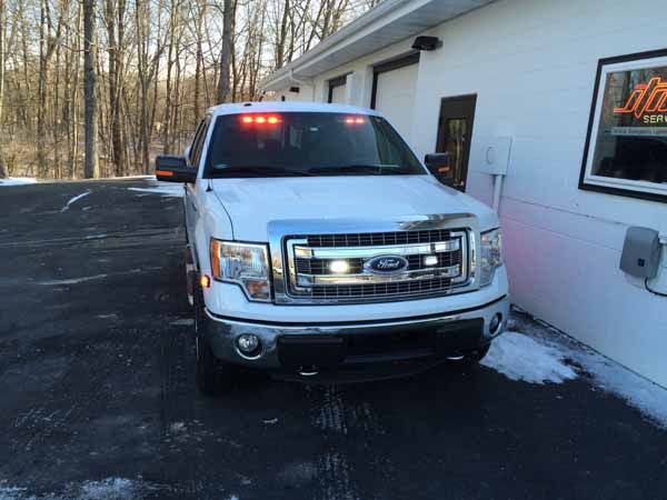 White Ford F-150 with flashing red lights parked near a building.