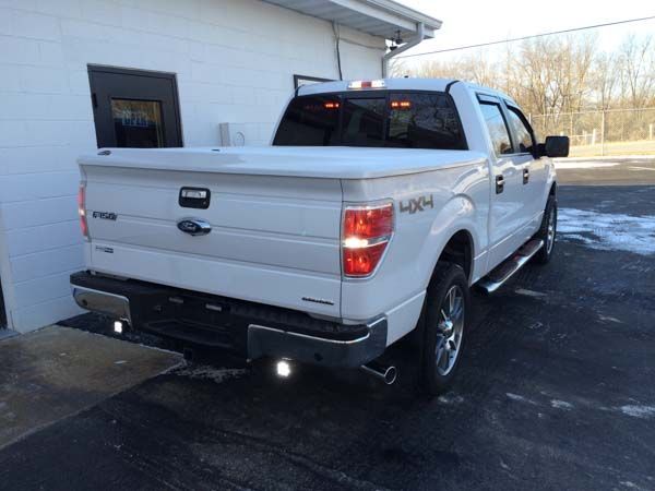 White Ford F-150 pickup truck with a white bed cover parked outside a building; 4x4 emblem visible.