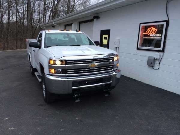 White Chevy pickup truck parked in front of a white building with an illuminated sign.