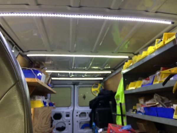 Inside of a work van with LED lighting, shelves with yellow bins, and the back doors visible.