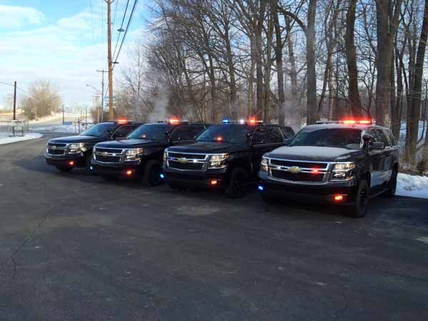 Four black police SUVs with flashing lights parked outdoors.