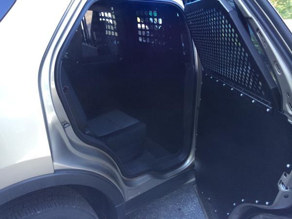 Open back door of a police SUV showing a caged back seat with a metal barrier.
