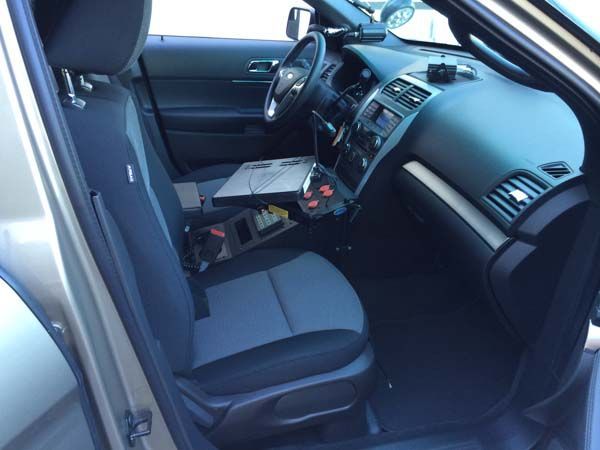 Interior view of a police car with computer, console, and driver's seat. Gray and black interior.