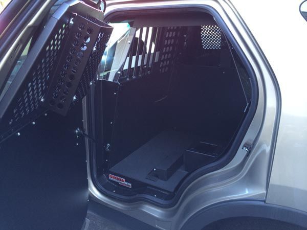 Open rear door of a police SUV, showing a prisoner transport compartment with metal bars and black interior.