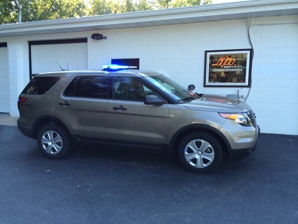 Brown police SUV with blue emergency lights parked in front of a white building.