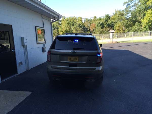 Rear view of a tan police SUV with blue emergency lights, parked next to a building.
