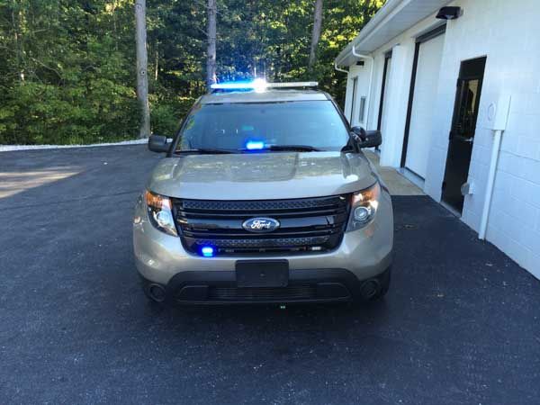 Tan police SUV with flashing blue lights parked near a white building.