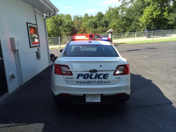 White Butler Police car with flashing red and blue lights, parked near a building.