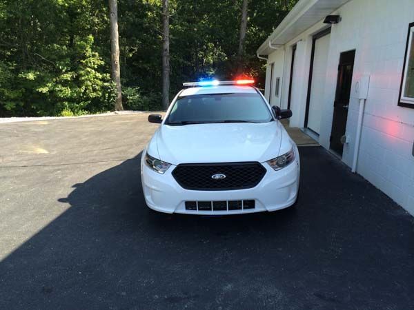 White police car parked near a building, emergency lights on.