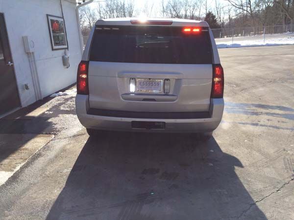 Silver SUV parked in front of a building on a sunny day; taillights are illuminated.