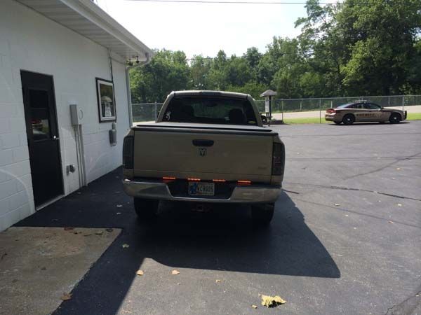Rear view of a tan pickup truck parked next to a white building; a police car is in the background.