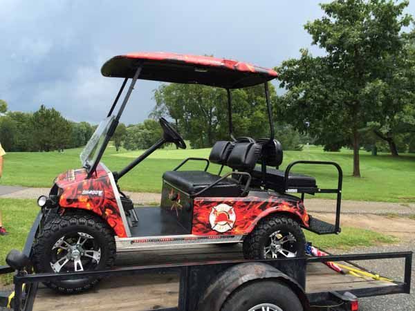 Red golf cart with flame design on trailer, parked on grass.