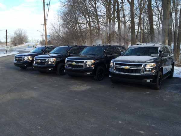 Four black SUVs parked on asphalt, snow in the background.