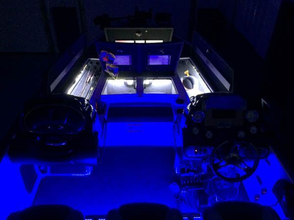 Dark room interior lit with blue lights. Boat control panel with two steering wheels and gauges.