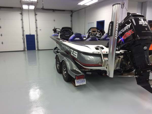 Bass boat with a Mercury engine parked in a garage with a glossy gray floor.