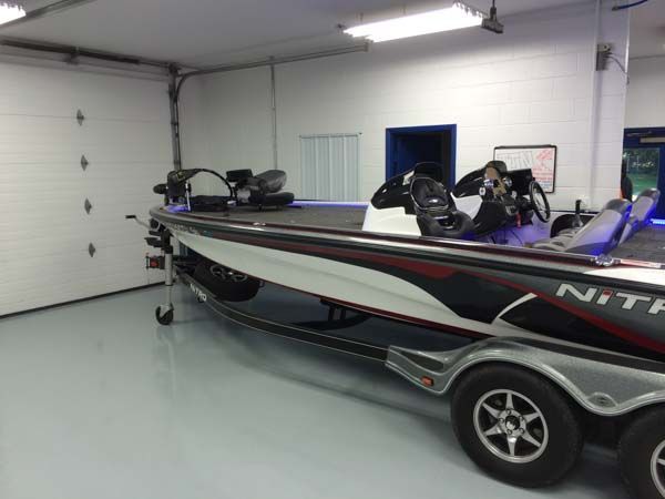 Bass boat on a trailer inside a garage with a closed white door and gray flooring.