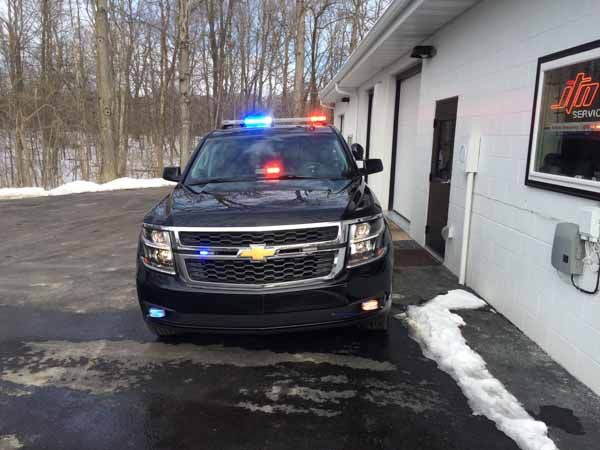 Black police SUV with flashing blue and red lights, parked in front of a building with a snow patch.