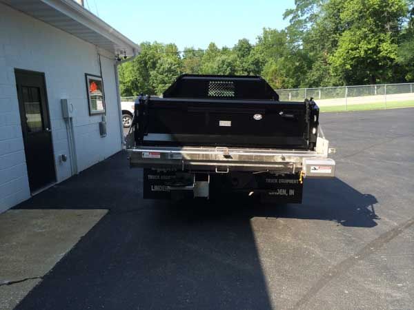 Black dump truck backed up next to a building on a paved lot.