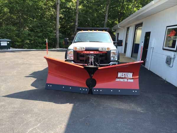 White snowplow truck with a red plow parked in front of a building.