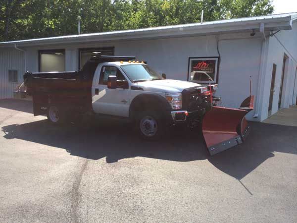 White pickup truck with snowplow parked in front of a white building.