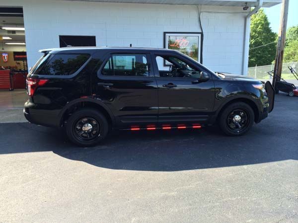Black police SUV parked in front of a building; features red emergency lights along the bottom.
