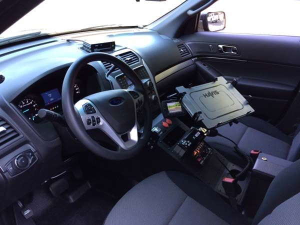 Interior of a police car with dashboard, steering wheel, and computer. Center console with various controls.