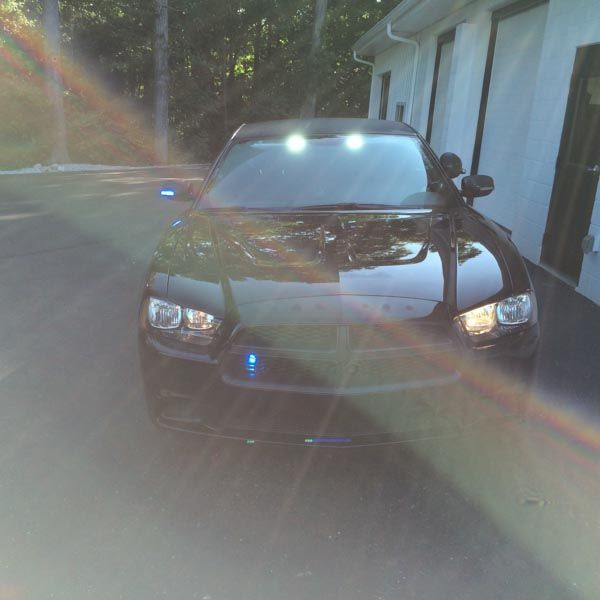 Black police car with blue and white lights parked in front of a building, sunlight flare.