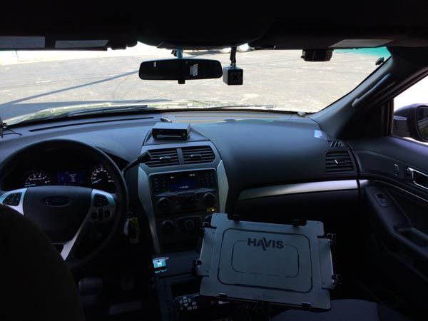Interior of a police car with dashboard, computer, and dashcam; viewed from the driver's seat.