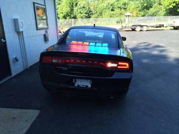 Black Dodge Charger with red and blue emergency lights, parked next to a building.