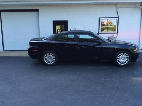 Black Dodge Charger parked in front of a white building with a garage door.