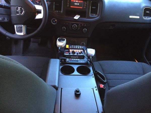 Interior of a police car with radio equipment and center console with cup holders. Dark interior with black dashboard.