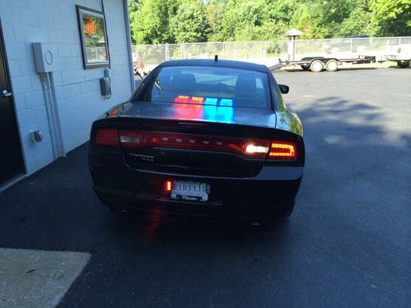 Black Dodge Charger with red and blue emergency lights, parked outside a building.