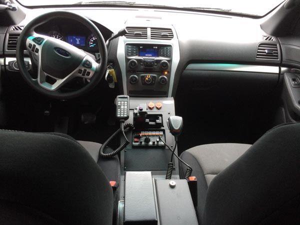 Interior view of a police car dashboard. Features radio, buttons, and steering wheel, with black and gray color scheme.