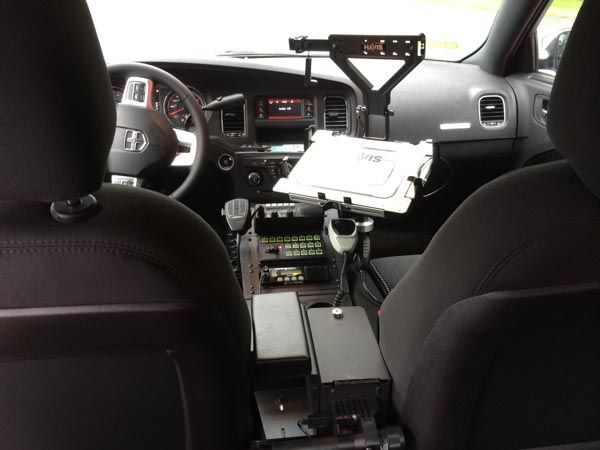 Interior of a police car with center console equipment, a tablet, and dashboard displays.