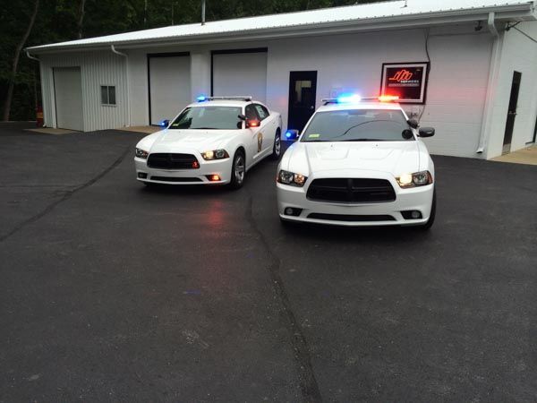 Two white police cars parked in front of a white building with lights flashing.