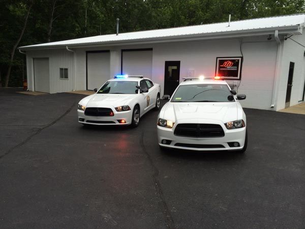 Two white police cars with flashing lights parked in front of a white building.