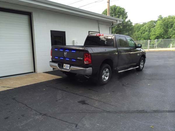 Dark pickup truck with blue lights parked near a white building with a garage door.
