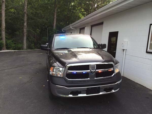 Dark gray Dodge pickup truck with flashing blue and red lights parked in front of a white building.