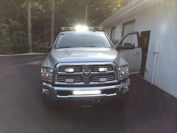 Gray Dodge truck with emergency lights parked next to a building, door open, bright sunlight.