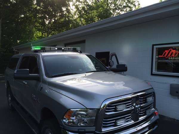 Silver Dodge truck with green lights parked outside a building with a window displaying the word “19”.