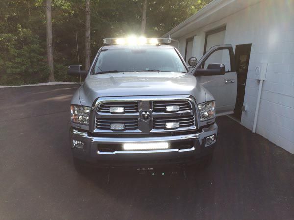 Silver Dodge truck with emergency lights parked in front of a white building with open door.