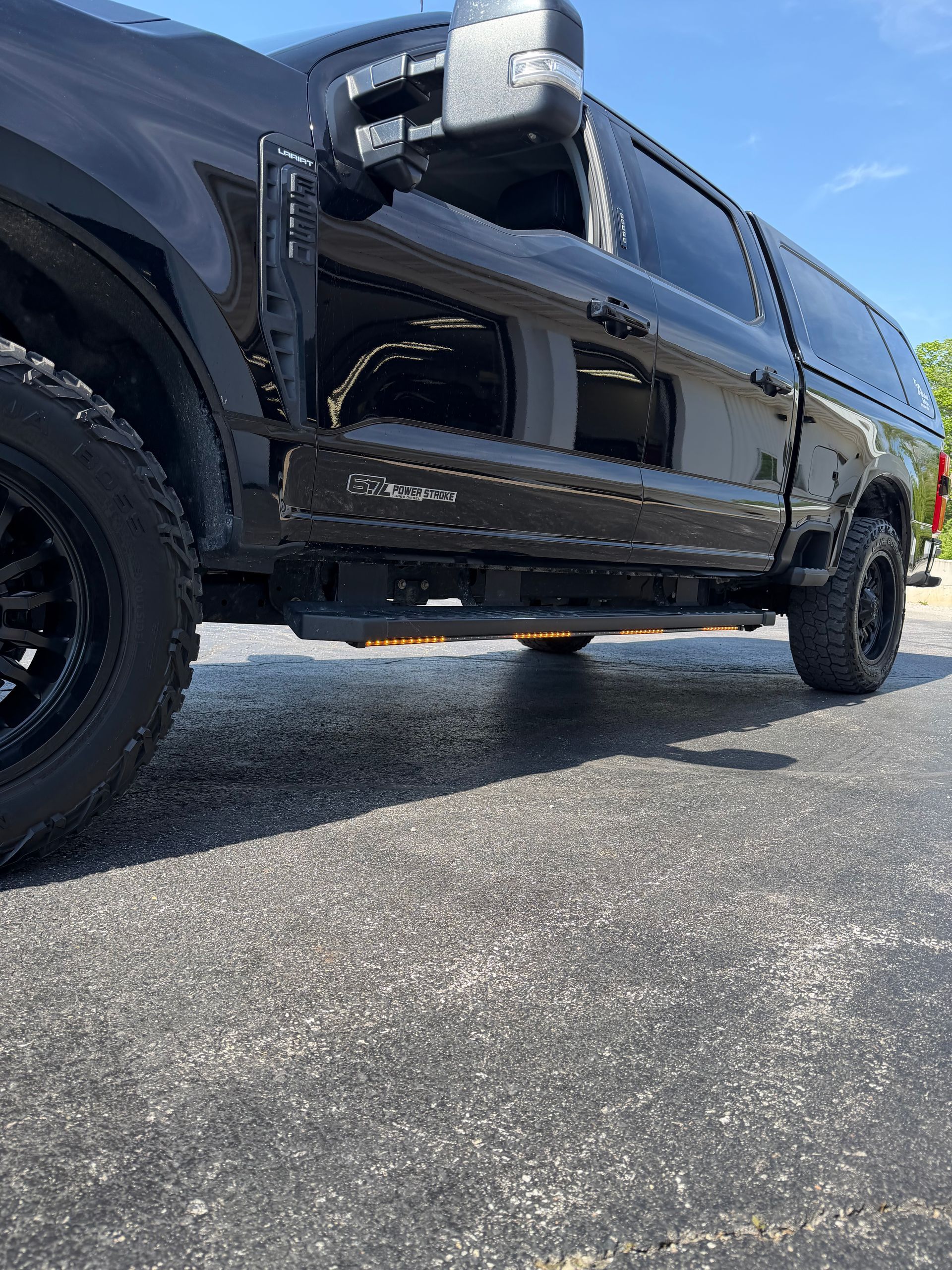 Black pickup truck parked on pavement, low-angle side view with chrome details and blue sky reflections