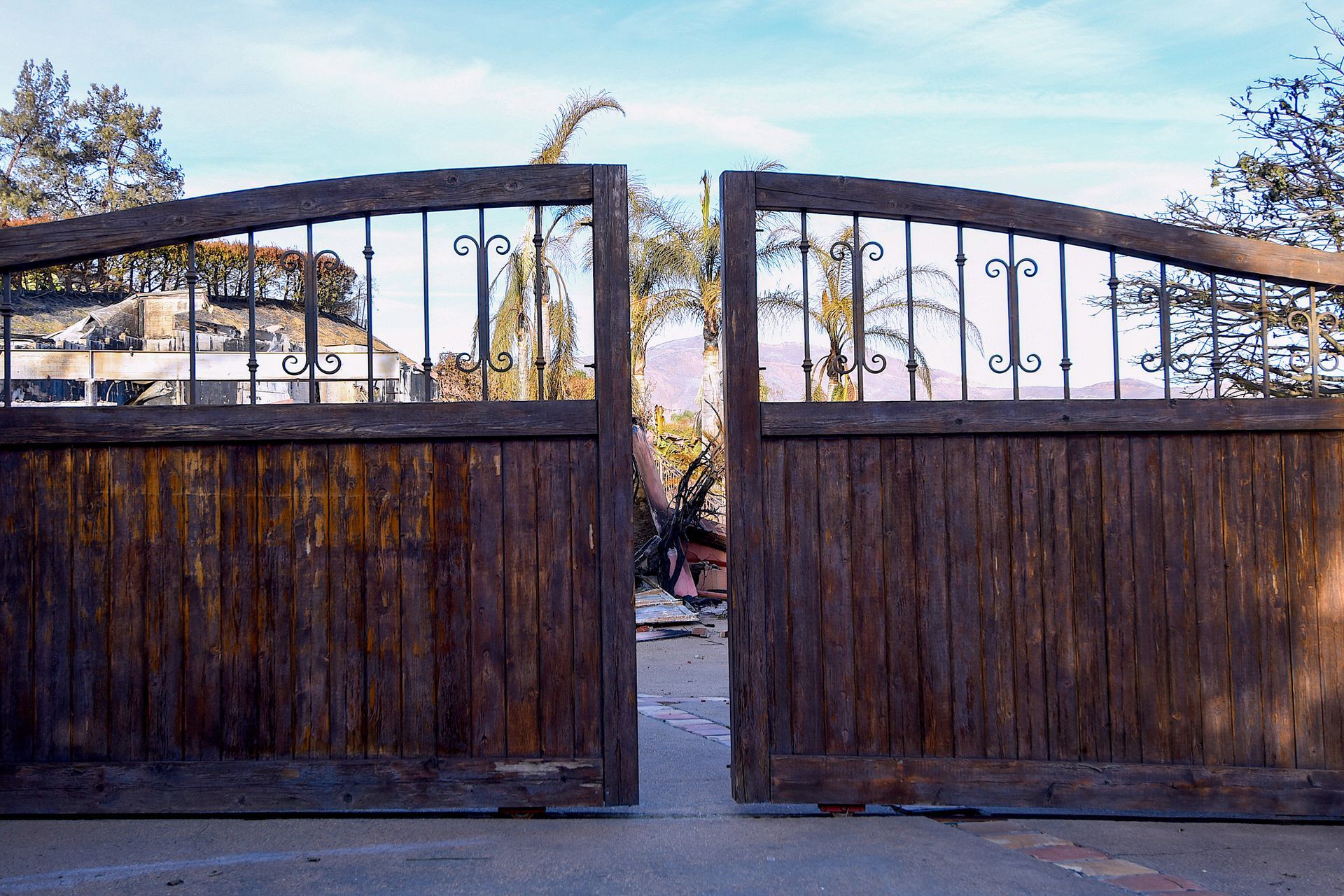 Charred trees and debris visible through open wooden gates post-fire.