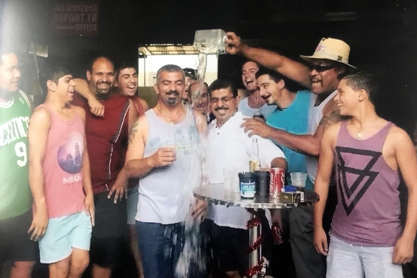 Group of men celebrating, water being poured on two men at a bar or outdoor setting.