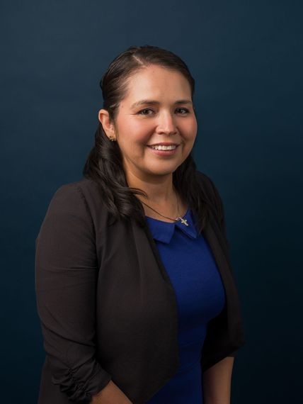 Studio portrait of a smiling woman in a black blazer over a blue top against a dark background