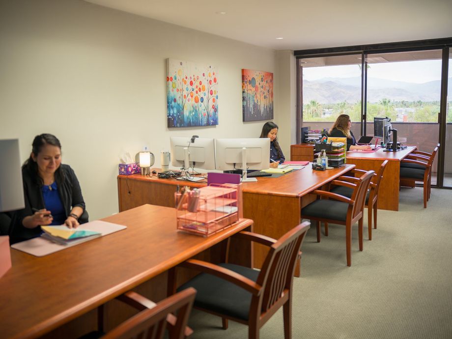 Office workspace with desks, computers, and two people working near a window with city and hill views