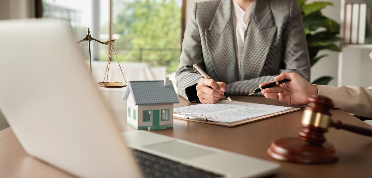 Lawyer at desk with scales, gavel, house model, and laptop in a bright office